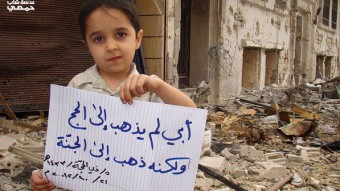 Menino segura cartaz com dizeres: “meu pai não foi ao Hajj (peregrinação à Meca), ele foi ao céu (indicando que o pai foi morto pelos bombardeios)” - Lens Young Homsi‎