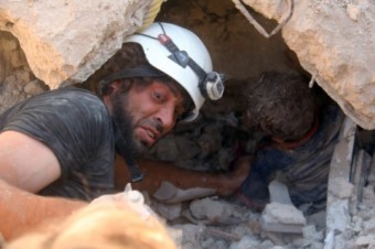 Homem tenta resgatar criança presa em um escombro após um atentado. Foto: Khaled Khatib/AFP