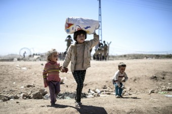 No sábado (20), crianças curdas levam pertences após cruzarem fronteira e chegarem à Turquia (Foto: Bulent Kilic/AFP)