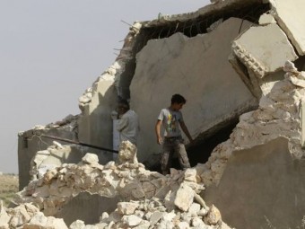 Menino junto com os destroços de um prédio danificado ao sul da periferia de Idlib, na Síria